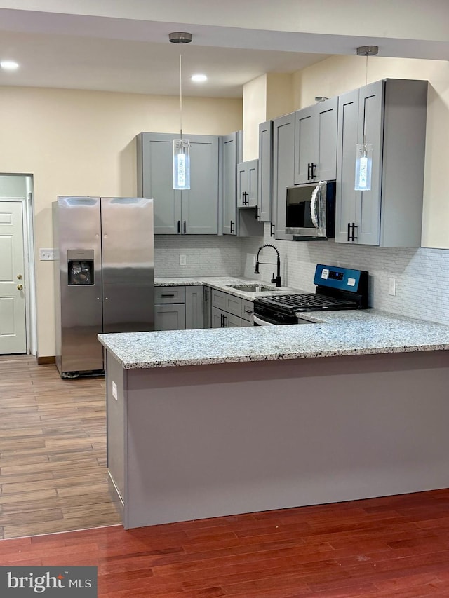 kitchen featuring stainless steel appliances, gray cabinets, a sink, and a peninsula