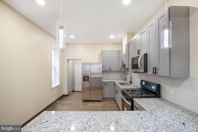 kitchen featuring tasteful backsplash, appliances with stainless steel finishes, light stone countertops, gray cabinets, and a sink