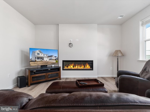 living room with baseboards, a glass covered fireplace, visible vents, and light wood-style floors