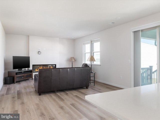 living area with light wood-type flooring, a glass covered fireplace, and baseboards