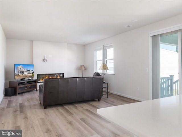 living room featuring light wood-type flooring, a glass covered fireplace, and baseboards