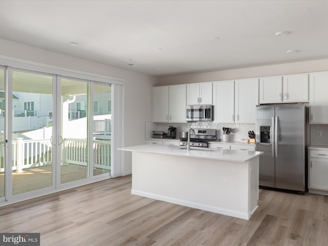 kitchen featuring tasteful backsplash, light countertops, appliances with stainless steel finishes, white cabinets, and an island with sink