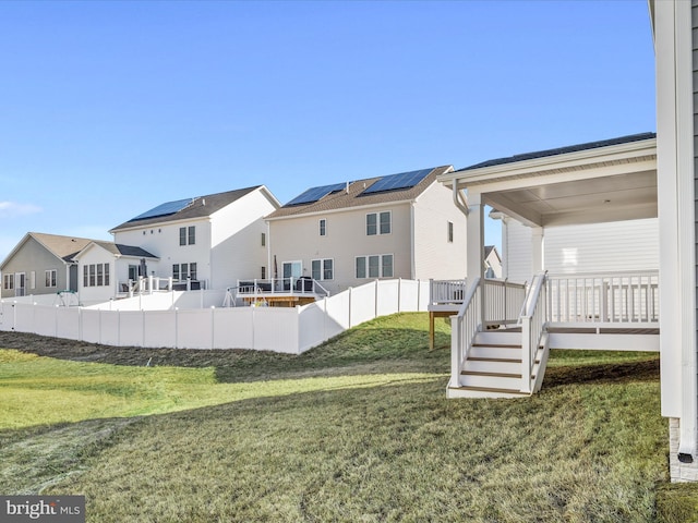 back of house featuring solar panels, a yard, fence, and a residential view