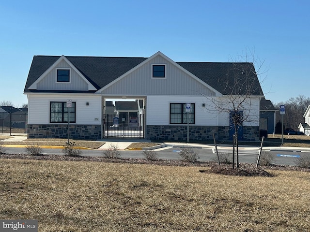 modern farmhouse style home featuring stone siding, a shingled roof, fence, and a front lawn