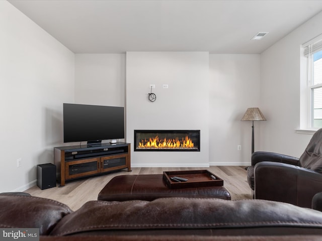 living area with light wood-type flooring, a glass covered fireplace, visible vents, and baseboards