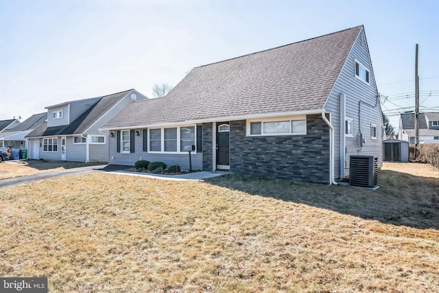 view of front of home featuring central AC, a front lawn, stone siding, and a shingled roof