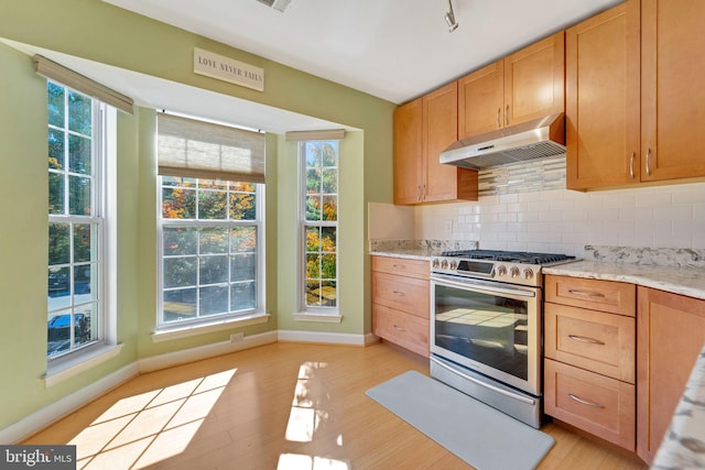 kitchen with tasteful backsplash, light wood-type flooring, stainless steel gas stove, and under cabinet range hood