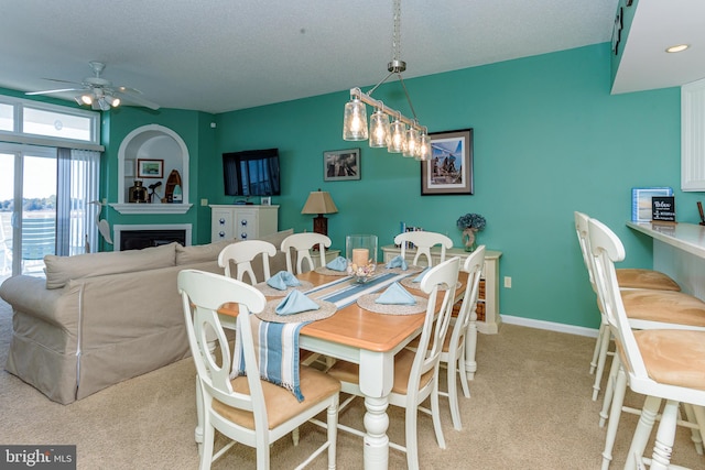 dining room with a fireplace, light carpet, ceiling fan, a textured ceiling, and baseboards