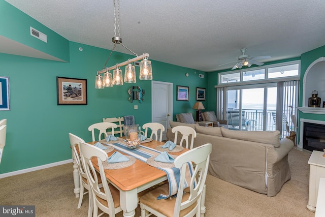 carpeted dining space with baseboards, visible vents, ceiling fan, a textured ceiling, and a fireplace