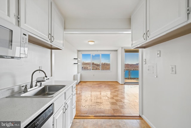 kitchen featuring white microwave, a sink, white cabinets, light countertops, and dishwasher