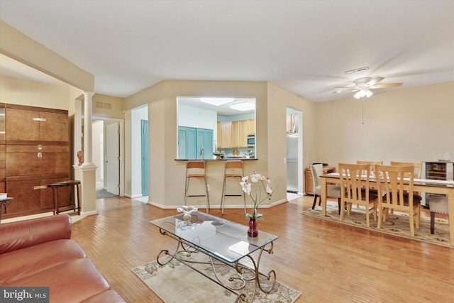 living area with ceiling fan, visible vents, baseboards, light wood-style floors, and decorative columns