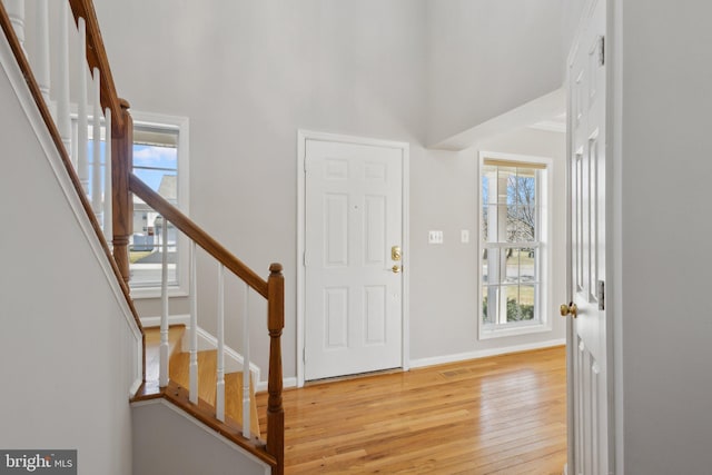 foyer entrance featuring stairway, baseboards, a high ceiling, and light wood-style flooring