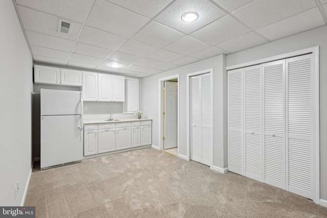 kitchen with visible vents, freestanding refrigerator, light countertops, white cabinetry, and light colored carpet