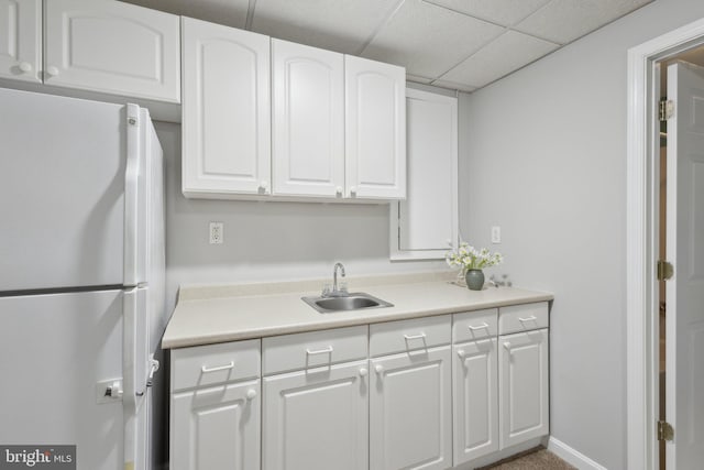 kitchen featuring a sink, freestanding refrigerator, white cabinets, light countertops, and a paneled ceiling