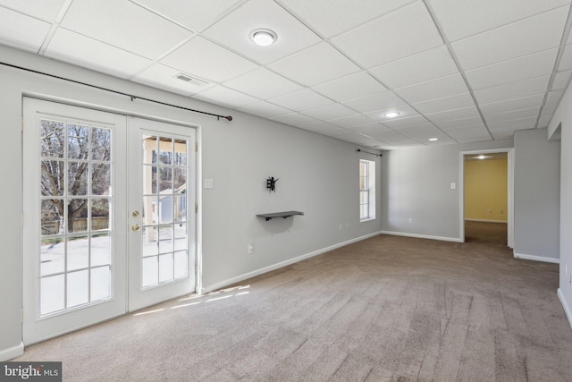 carpeted empty room with french doors, baseboards, and a drop ceiling