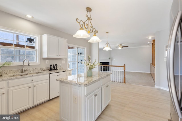 kitchen featuring a kitchen island, a fireplace, white dishwasher, a sink, and white cabinetry