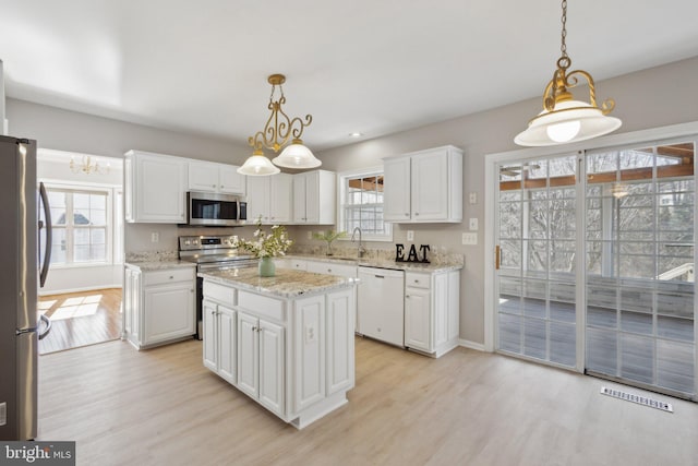 kitchen featuring light wood finished floors, a center island, white cabinets, stainless steel appliances, and a sink