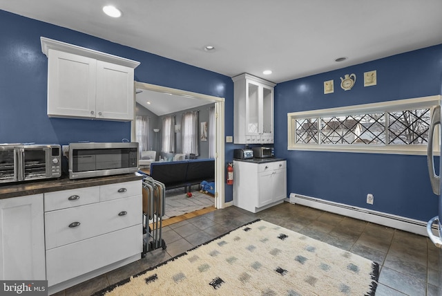 kitchen featuring a baseboard heating unit, dark countertops, stainless steel microwave, and white cabinetry