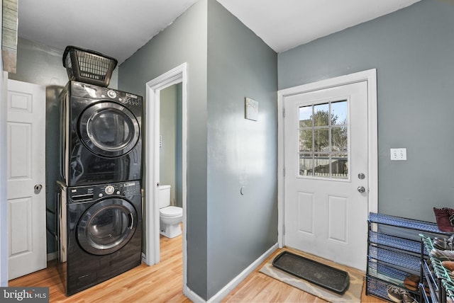 laundry room featuring laundry area, baseboards, wood finished floors, and stacked washer and clothes dryer