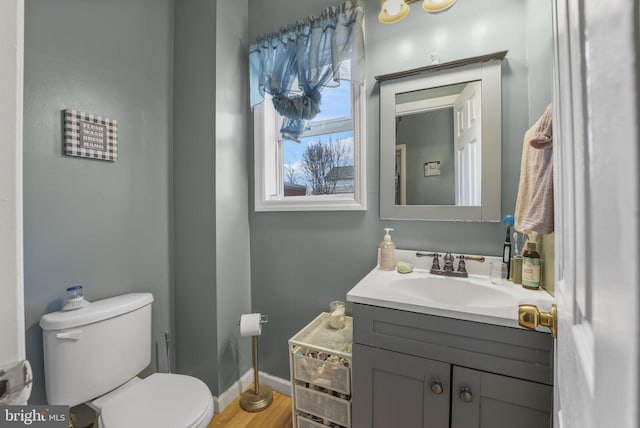 bathroom featuring toilet, baseboards, wood finished floors, and vanity