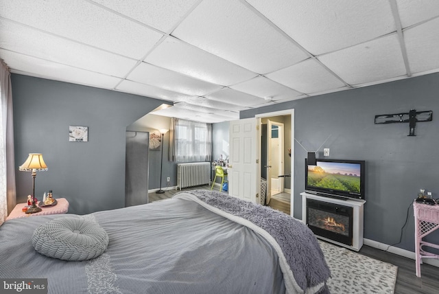 bedroom featuring baseboards, a drop ceiling, radiator heating unit, and wood finished floors