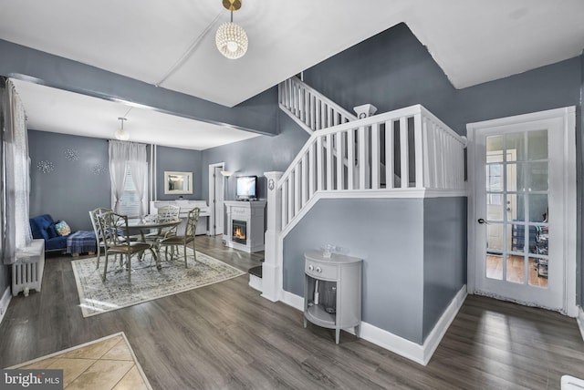 dining area featuring dark wood-style floors, radiator heating unit, a lit fireplace, baseboards, and stairs