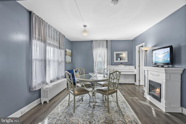 dining area with a glass covered fireplace, dark wood-style flooring, baseboards, and radiator heating unit