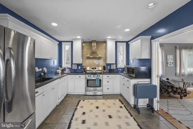 kitchen with wall chimney exhaust hood, appliances with stainless steel finishes, dark countertops, and white cabinetry