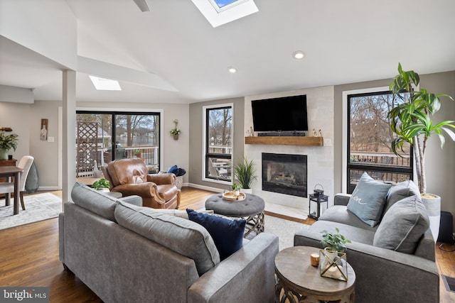 living area featuring a large fireplace, lofted ceiling with skylight, wood finished floors, and baseboards