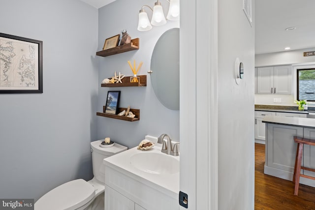 bathroom with toilet, recessed lighting, wood finished floors, vanity, and an inviting chandelier