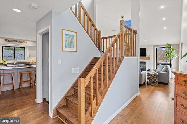 stairway with recessed lighting, visible vents, hardwood / wood-style floors, and a glass covered fireplace