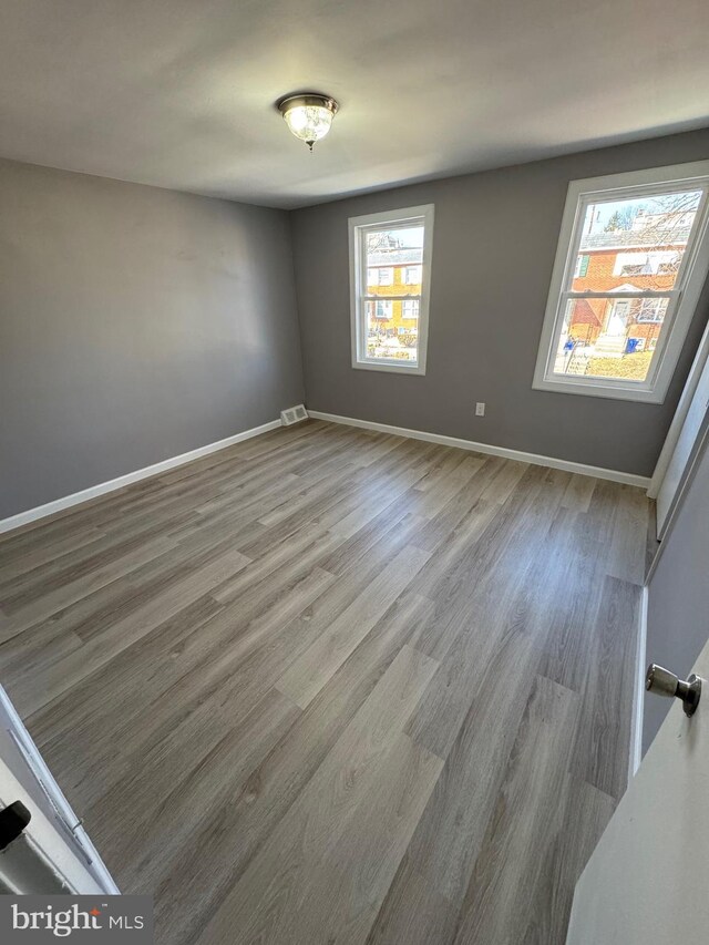 unfurnished room with plenty of natural light, baseboards, visible vents, and wood finished floors