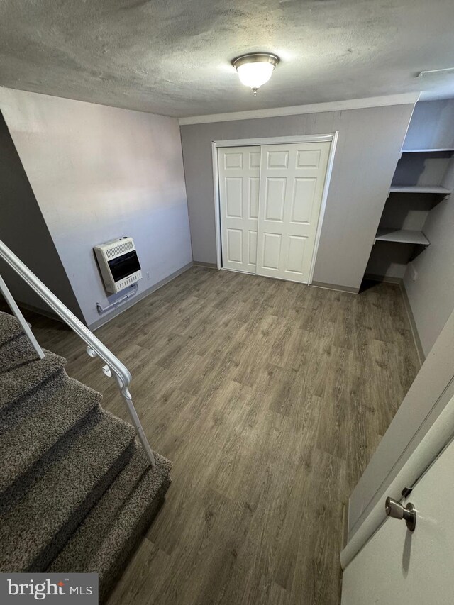 stairway with heating unit, wood finished floors, baseboards, and a textured ceiling