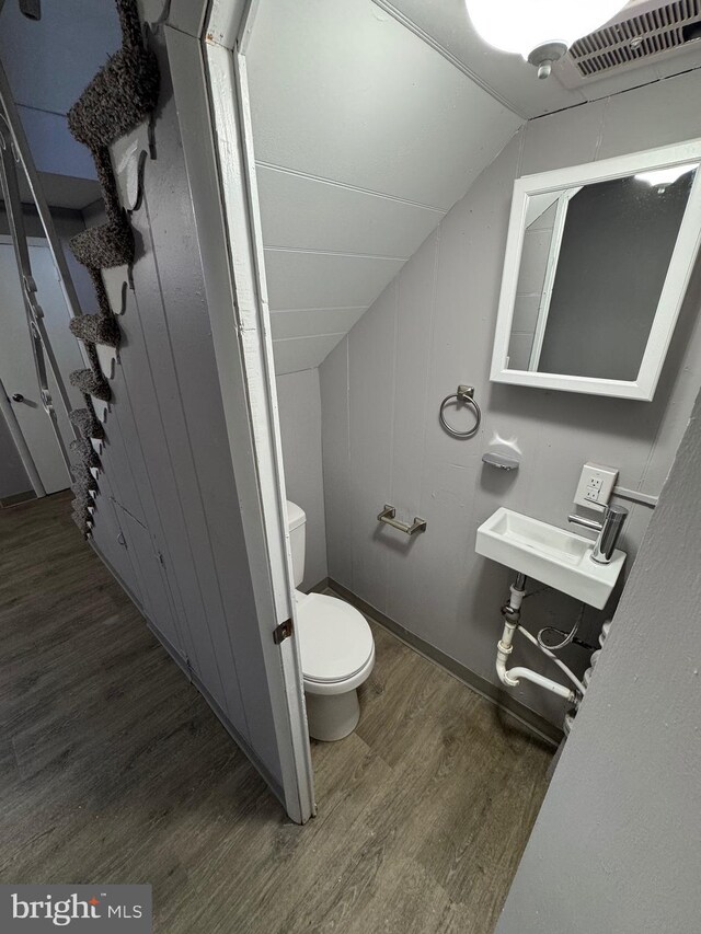 half bath featuring vaulted ceiling, toilet, visible vents, and wood finished floors