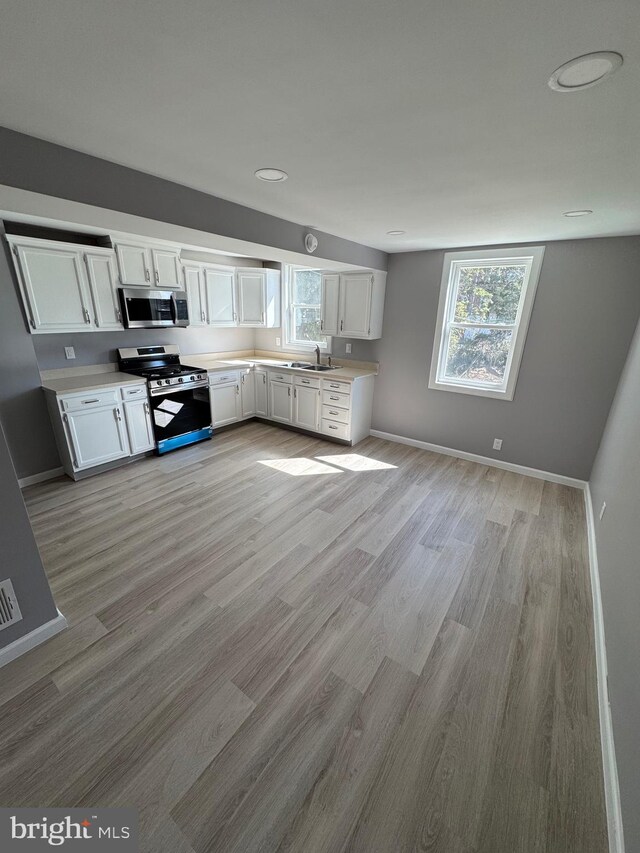 kitchen with a sink, stainless steel appliances, white cabinets, and light countertops