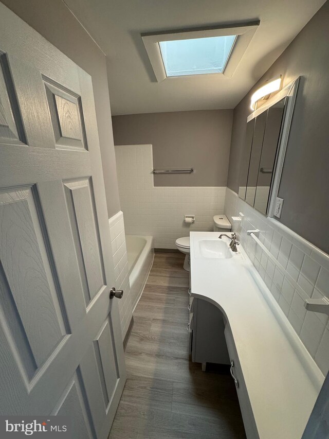 full bathroom with vanity, a bathing tub, a skylight, tile walls, and toilet