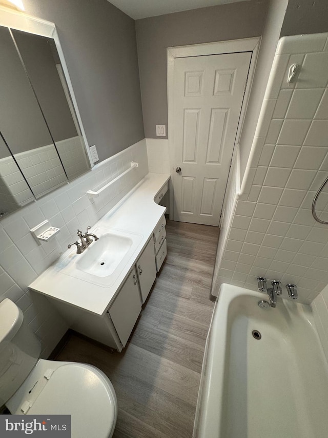 bathroom with vanity, a bath, wood finished floors, tile walls, and toilet
