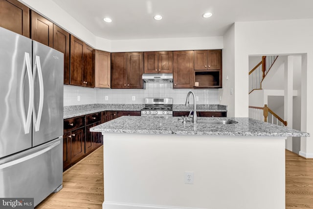 kitchen featuring appliances with stainless steel finishes, an island with sink, and light stone countertops