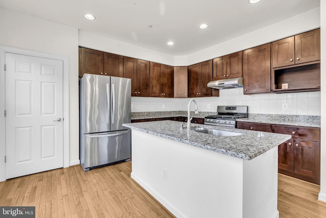 kitchen featuring appliances with stainless steel finishes, light wood-type flooring, under cabinet range hood, and light stone countertops