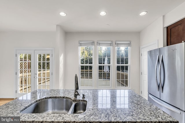 kitchen with recessed lighting, light stone counters, a sink, and freestanding refrigerator