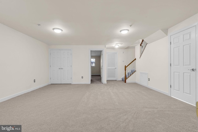 finished below grade area featuring light carpet, stairway, and baseboards