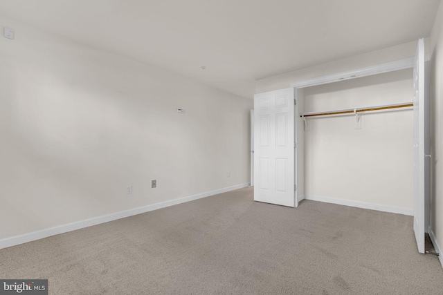 unfurnished bedroom featuring light carpet, baseboards, and a closet