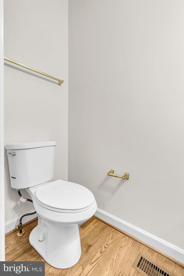 half bath featuring toilet, visible vents, baseboards, and wood finished floors