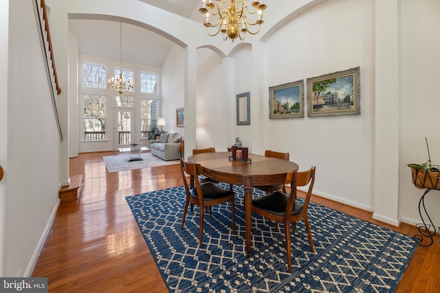 dining room featuring a towering ceiling, baseboards, a chandelier, and hardwood / wood-style floors