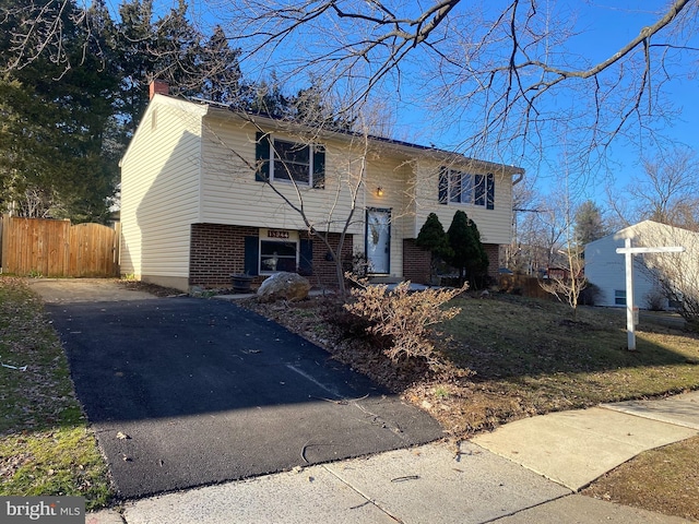 raised ranch with driveway, fence, and brick siding