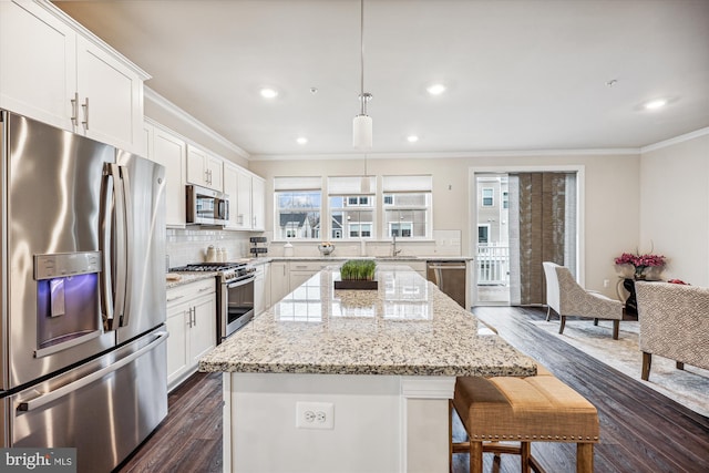 kitchen with appliances with stainless steel finishes, white cabinets, ornamental molding, and a breakfast bar area