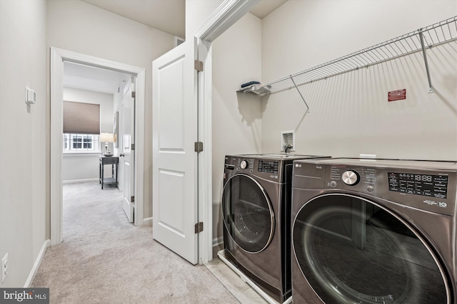 clothes washing area featuring laundry area, light colored carpet, baseboards, and washing machine and clothes dryer