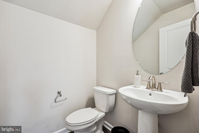 half bathroom featuring toilet, baseboards, vaulted ceiling, and a sink