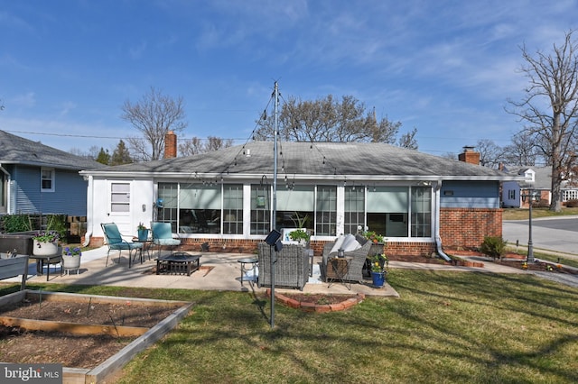 rear view of property featuring a lawn, a fire pit, brick siding, a chimney, and a patio area