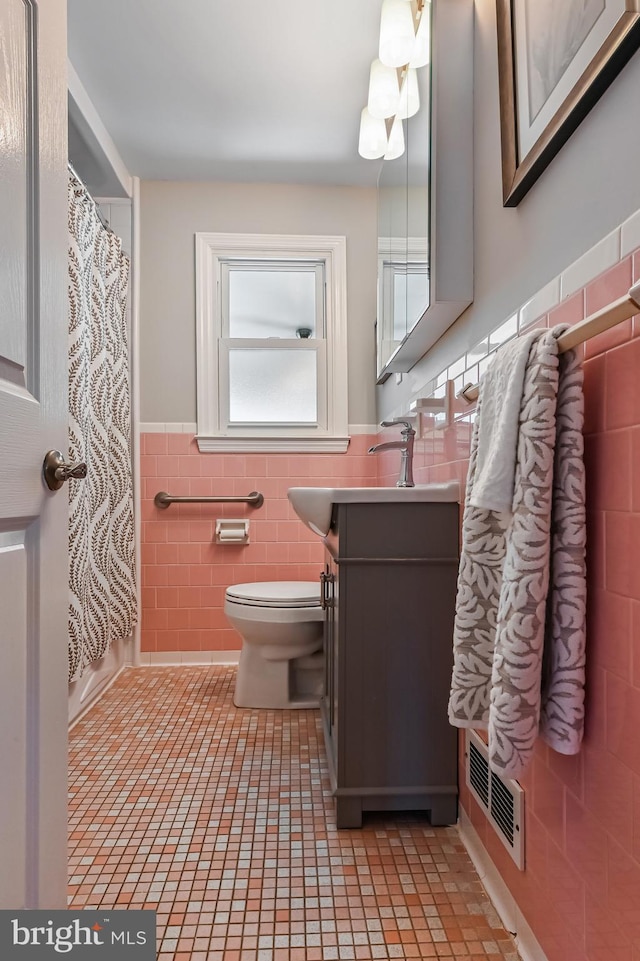 bathroom with visible vents, a wainscoted wall, toilet, vanity, and tile walls